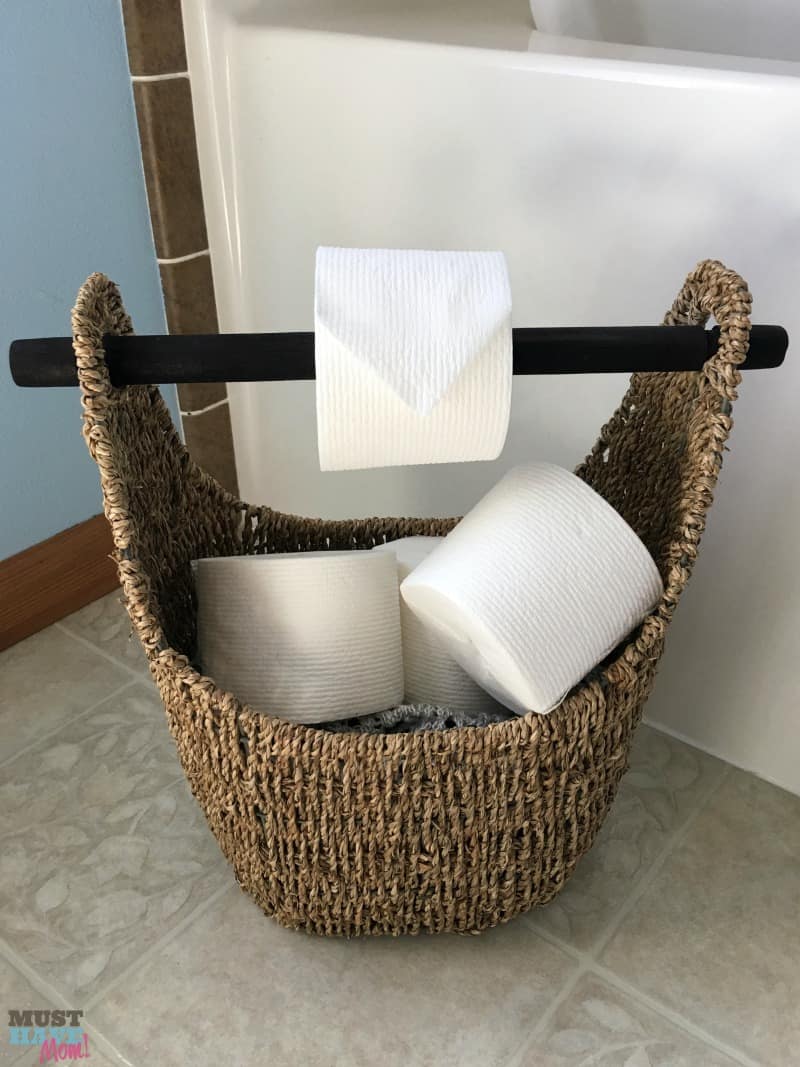 DIY toilet paper holder idea! Use a wicker basket with a wood handle as a toilet paper holder and fill the basket with extra toilet paper rolls. Works with tube free toilet paper rolls too!