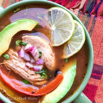 chicken fajita soup in a bowl with avocado, limes and garnish